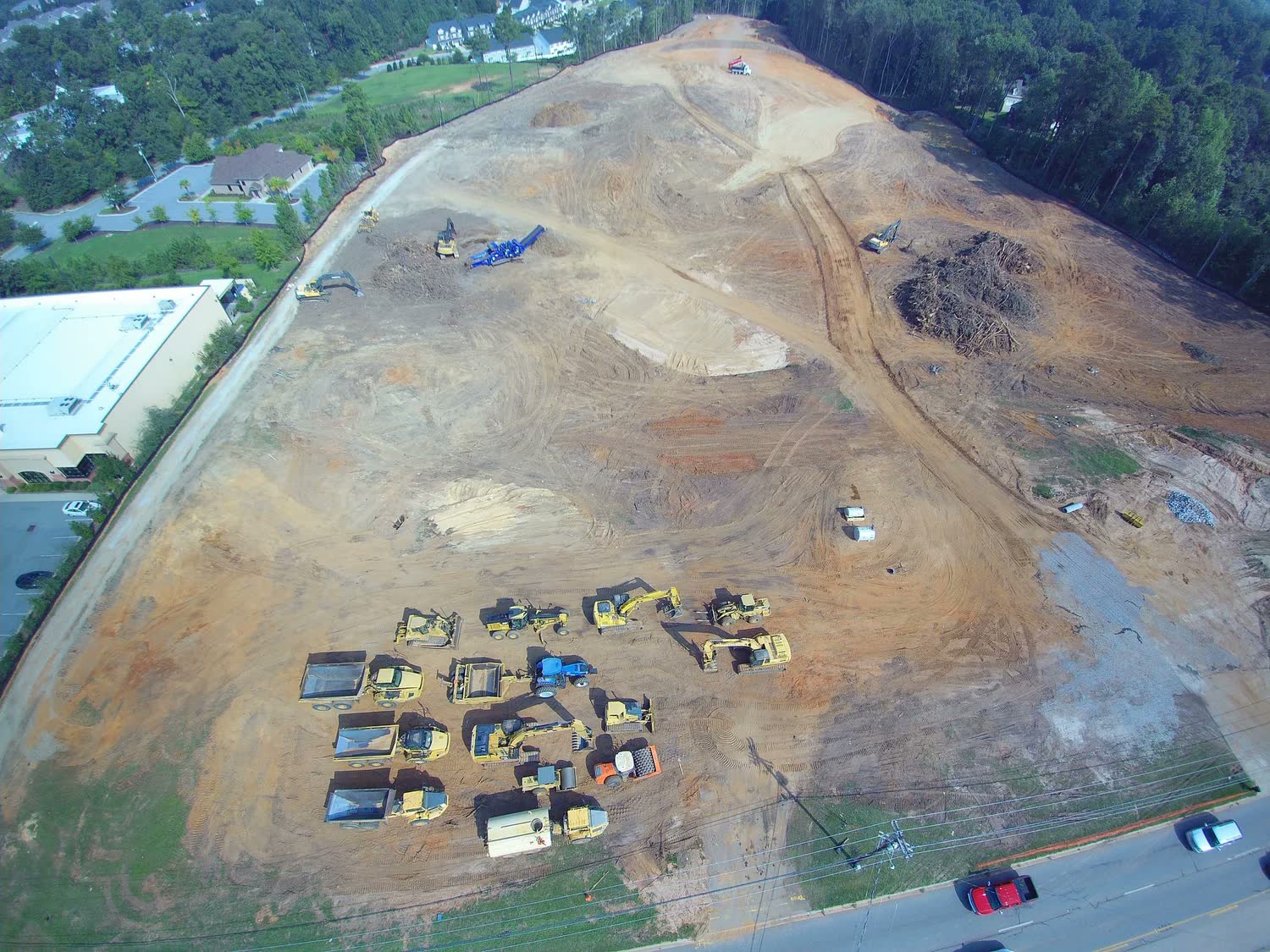 Cleared commercial site with an excavator working the initial grade and a building in the background.